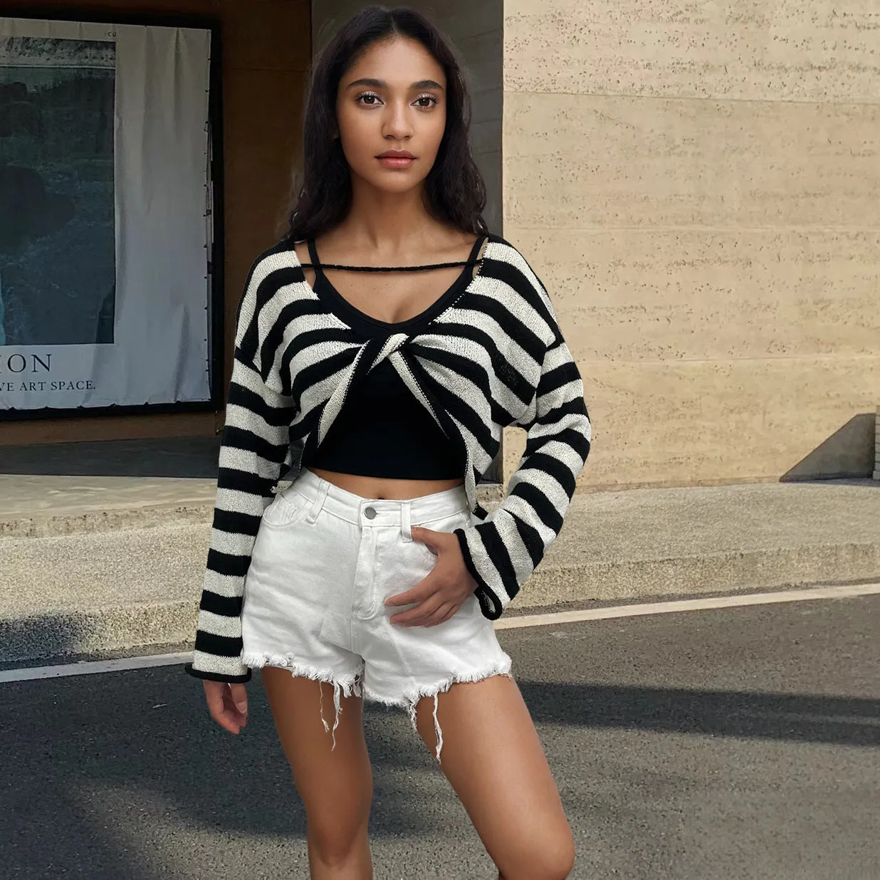 A woman wearing a cropped black and white striped long-sleeved sweater with a front and back exposed-navel design.