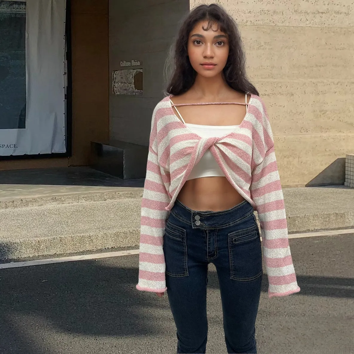 A woman wearing a cropped black and white striped long-sleeved sweater with a front and back exposed-navel design.