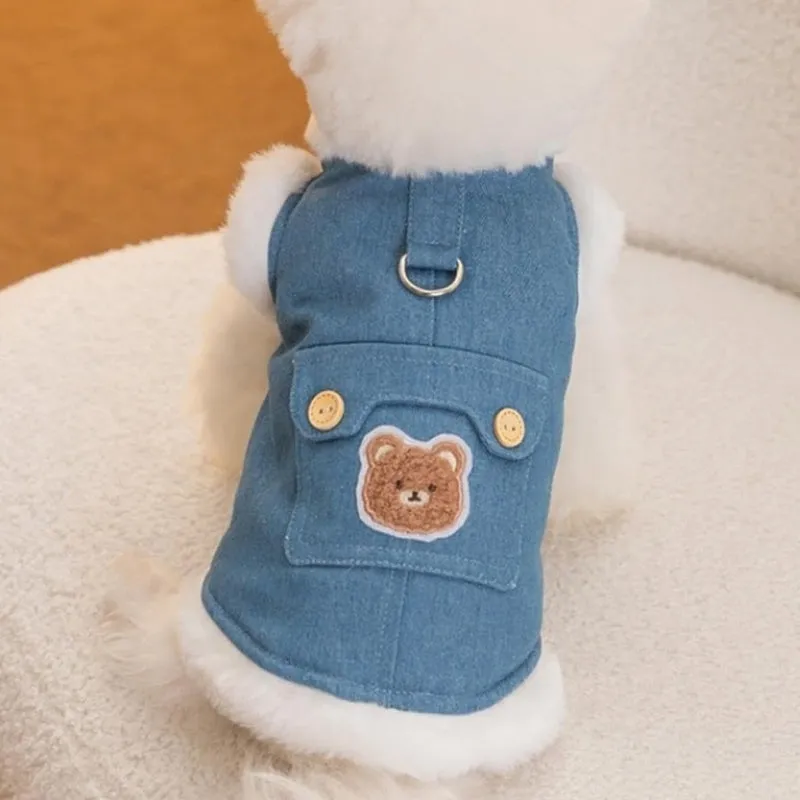 Denim dog vest with white wool lining, embroidered teddy bear patches, wooden buttons, and metal D-ring on blue background