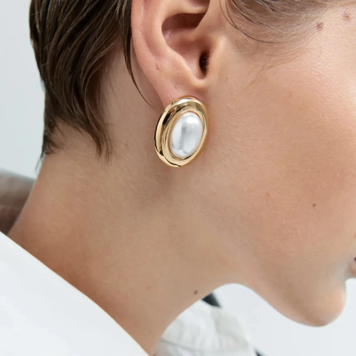 Close-up of a pair of women's stainless steel vintage pearl ear studs with a silver-toned post on a white background.
