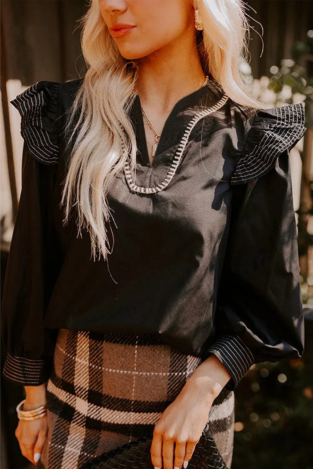 Black women's V-neck blouse with long ruffle sleeves and contrast white stitching on seams.