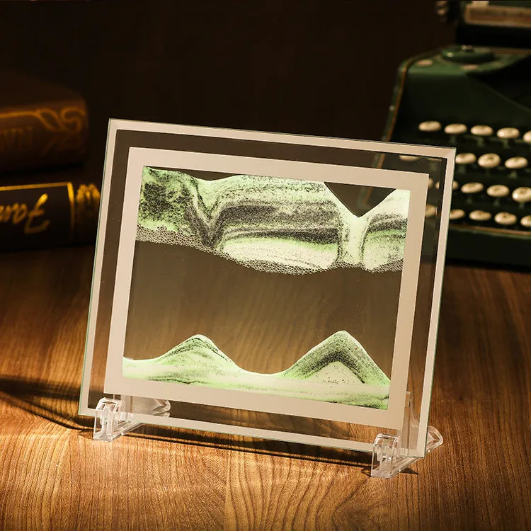 Geometric glass ornament with shifting coloured quicksand inside, shown in black and white with green accents.