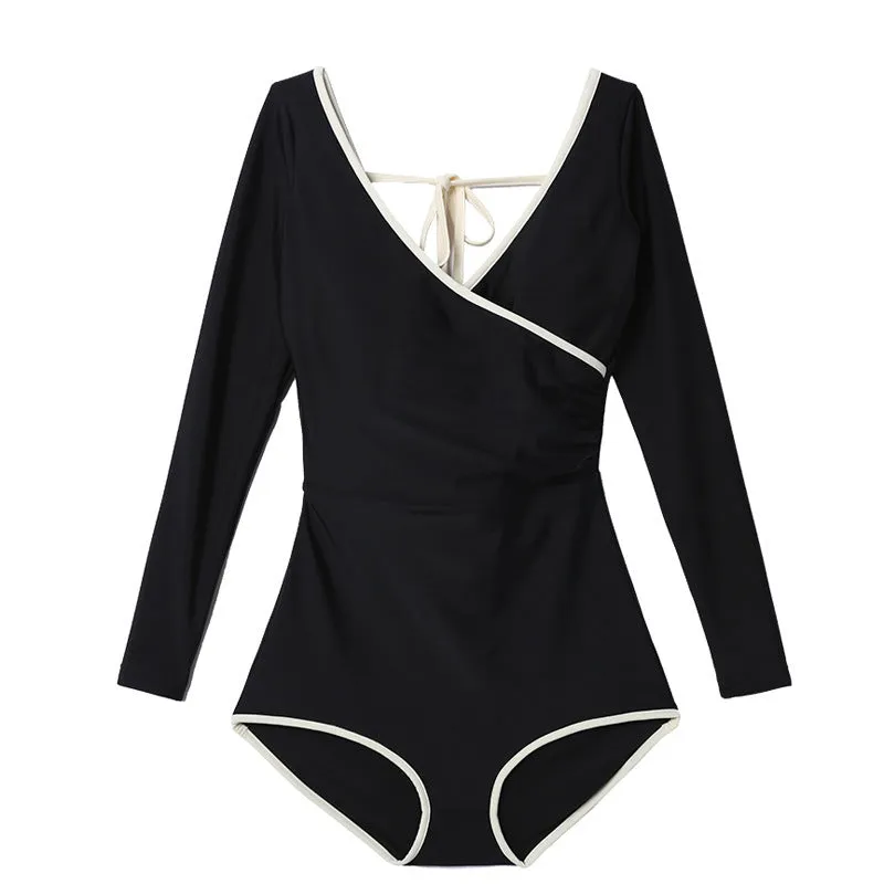 Women’s long sleeve conservative one-piece swimsuit in solid black with white edge trim on a model.