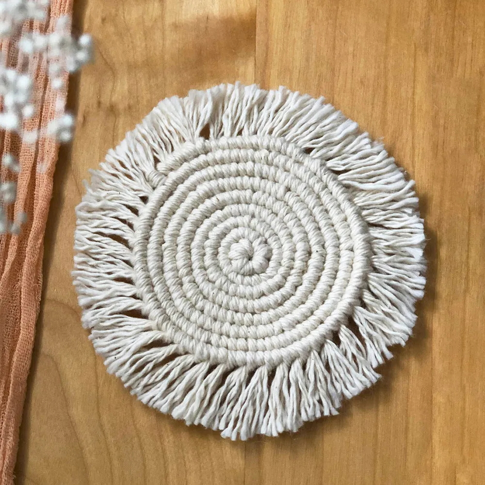 Hand-woven round beige cotton string coaster on a wooden table with a glass of water