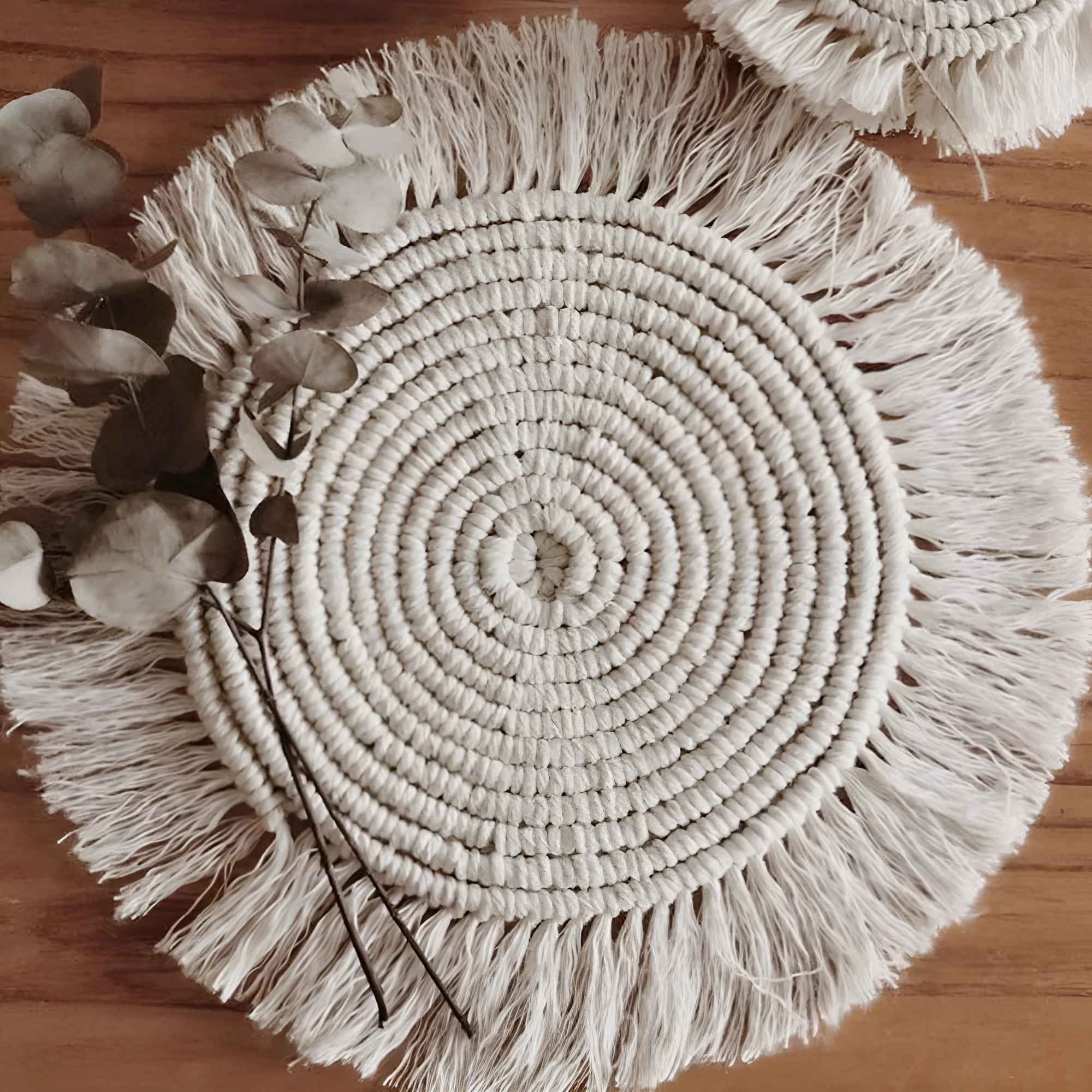 Hand-woven round beige cotton string coaster on a wooden table with a glass of water