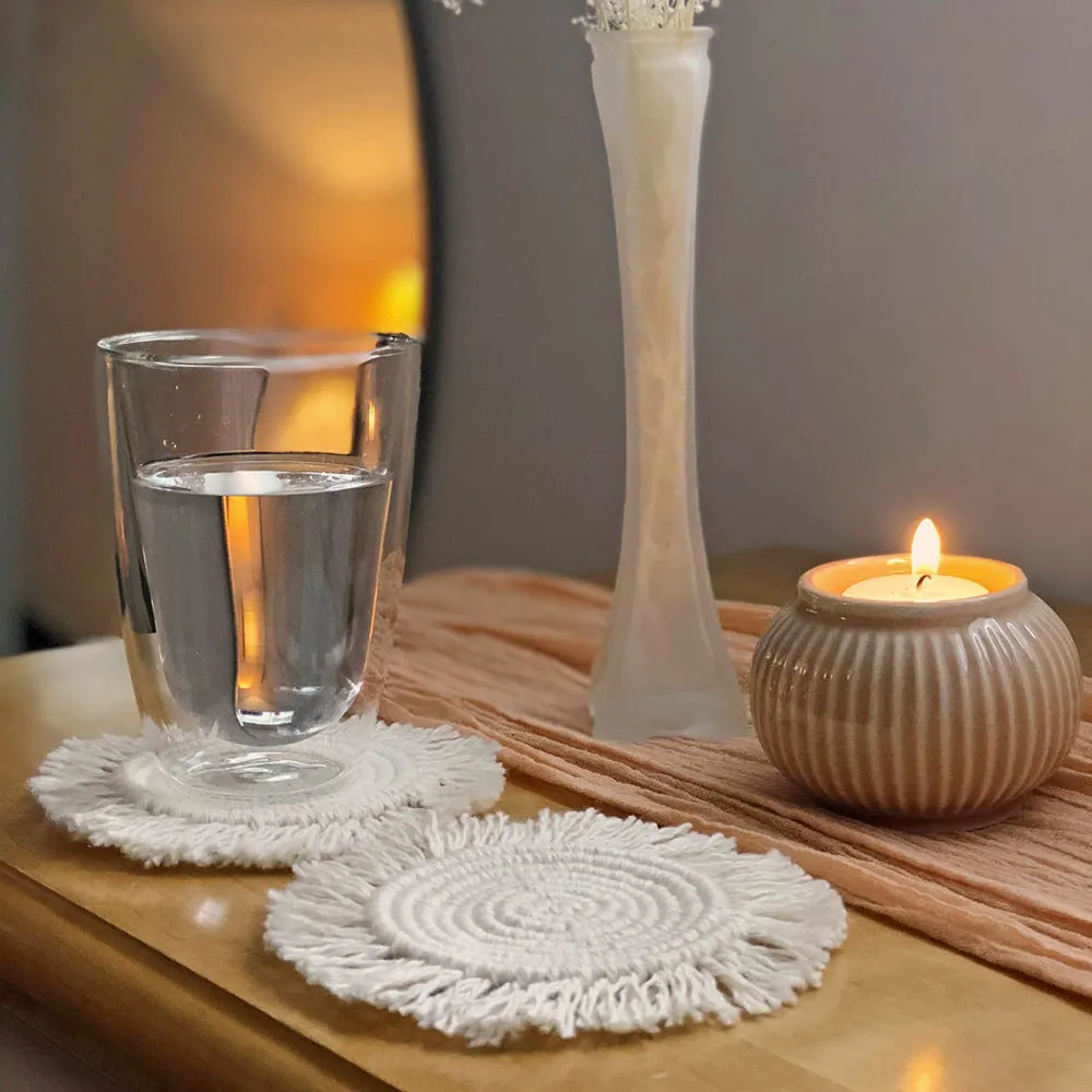 Hand-woven round beige cotton string coaster on a wooden table with a glass of water