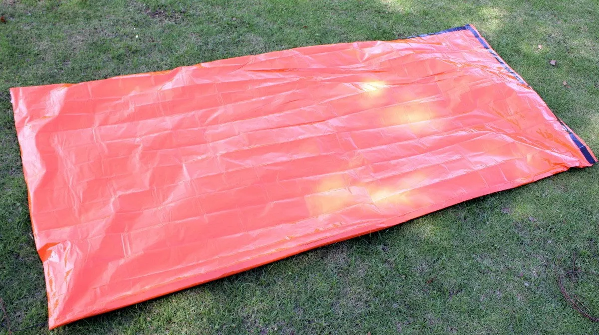 Orange PE aluminium film emergency sleeping bag folded and laid flat on outdoor ground