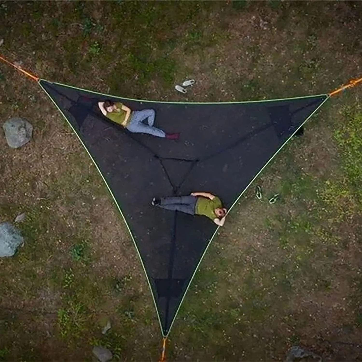 Black polyester portable multi-person triangle hammock lying on grass with trees in background