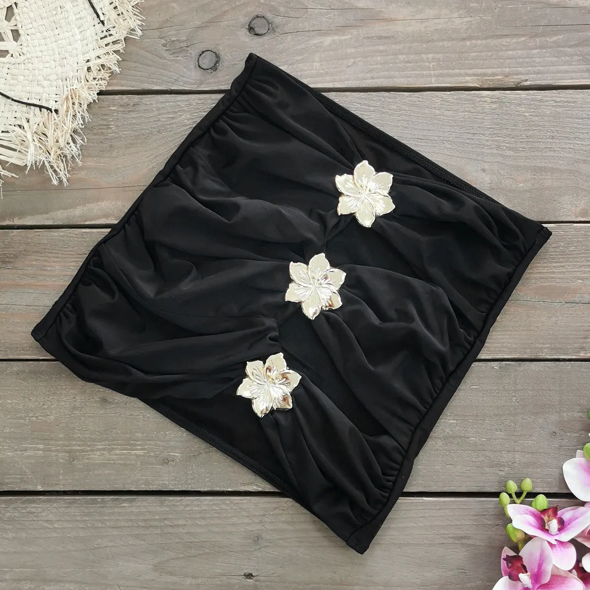 Women's black hollow-out tube top one-piece swimsuit with matching high-waist short skirt laid flat.