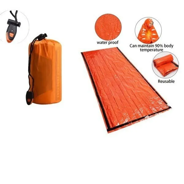 Orange aluminium foil emergency sleeping bag with drawstring bag and whistle on ground
