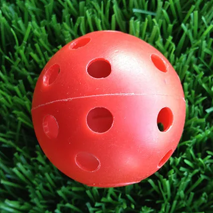 Hollow plastic golf practice ball in orange colour on indoor surface