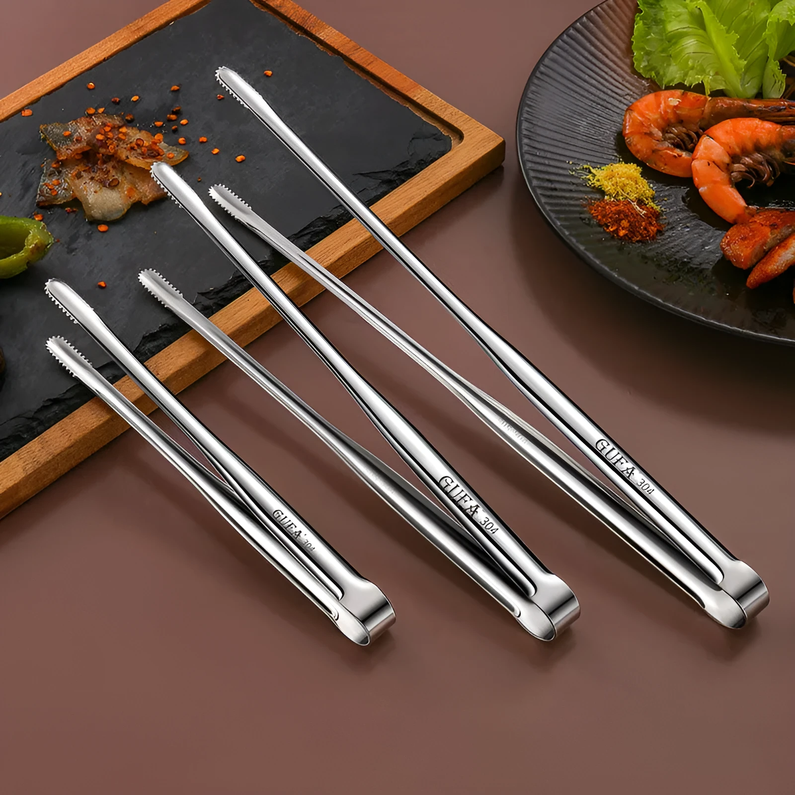 Stainless steel barbecue clamp in modern simple design on a table, showing the three size options small medium large