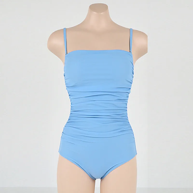 Sling style one-piece swimsuit with belly pleats in black, blue, white, or yellow on a model