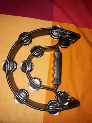 Double moon shaped black plastic tambourine with handle, 25 x 20 cm, on a light background