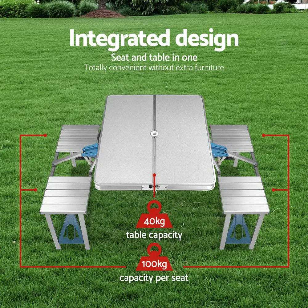 Outdoor folding table and chair set in aluminium alloy with four chairs, expanded on grass, silver gray colour, showing 85.5cm desktop and umbrella hole