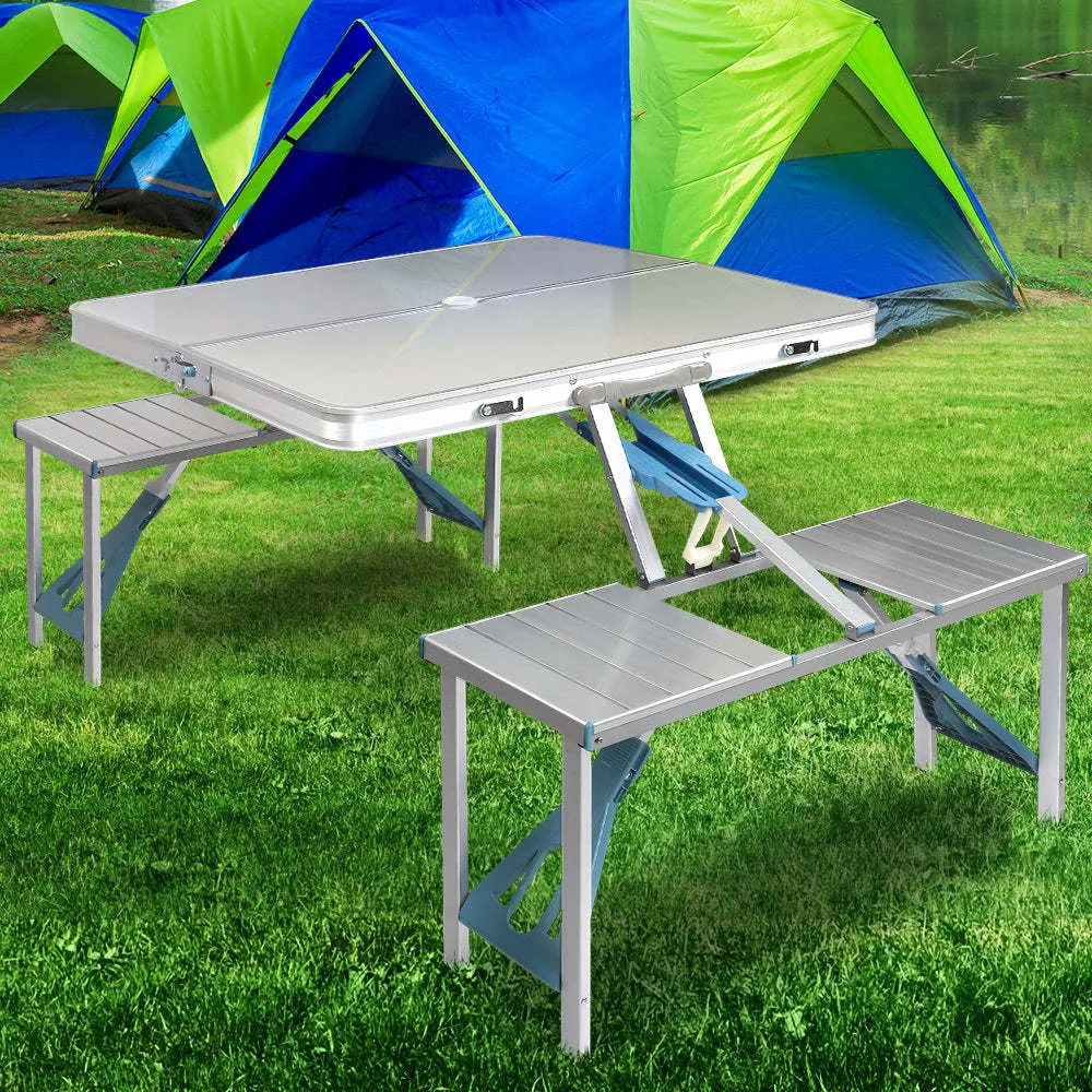 Outdoor folding table and chair set in aluminium alloy with four chairs, expanded on grass, silver gray colour, showing 85.5cm desktop and umbrella hole