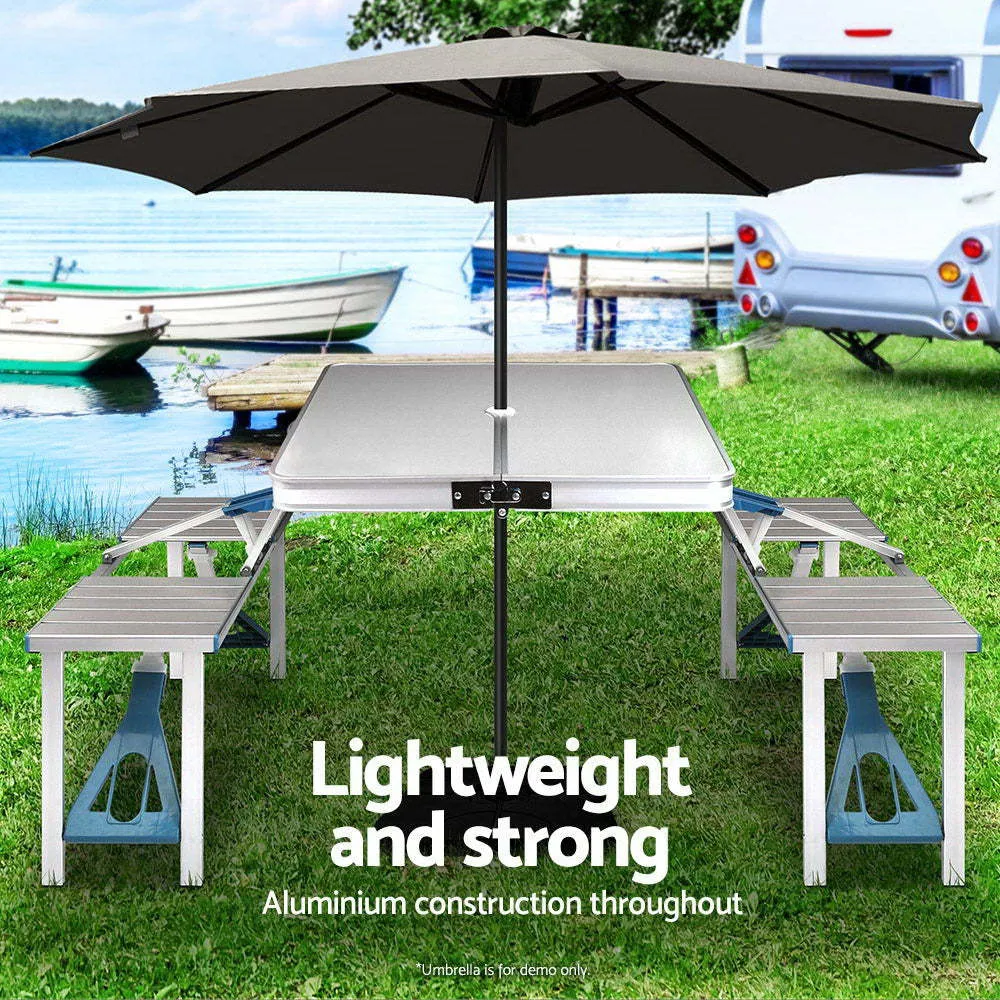 Outdoor folding table and chair set in aluminium alloy with four chairs, expanded on grass, silver gray colour, showing 85.5cm desktop and umbrella hole