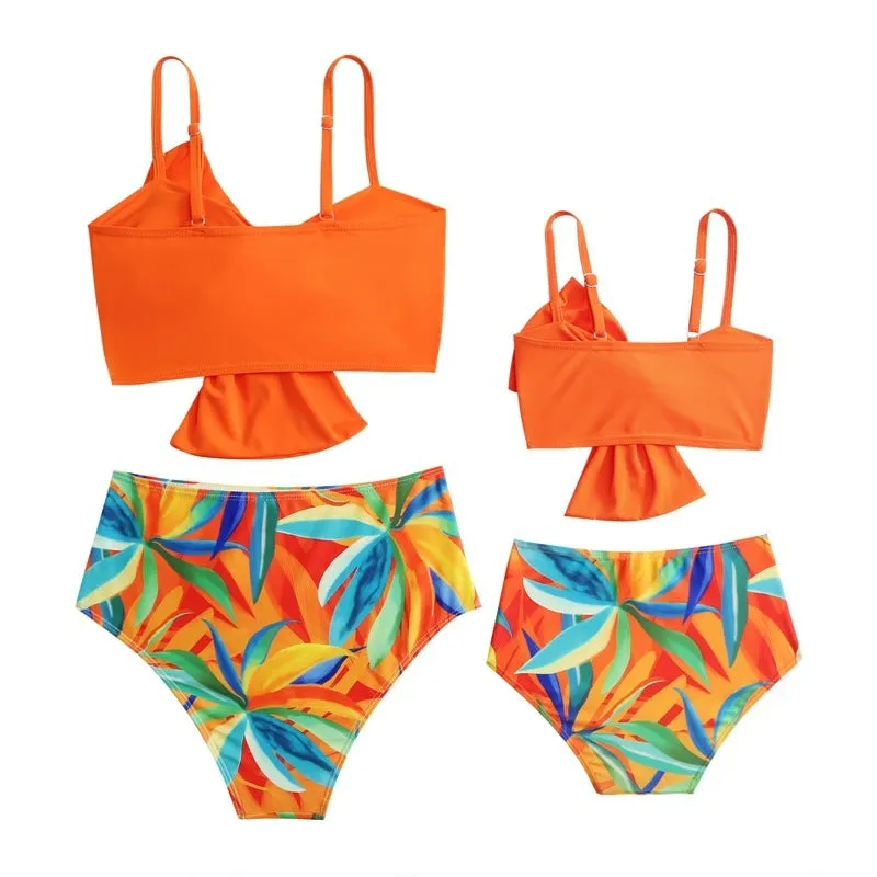 Women's orange nylon bikini set with large white bow print, showing top and swim trunks.