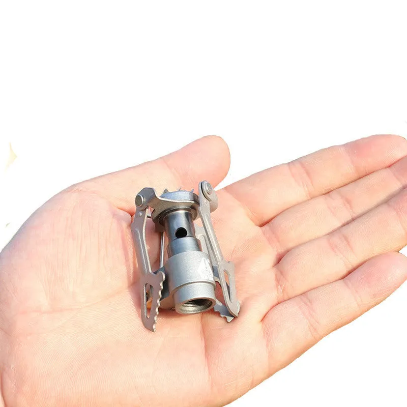 Compact one-piece propane camping stove on rocky ground, fuel canister attached, with a pot boiling.