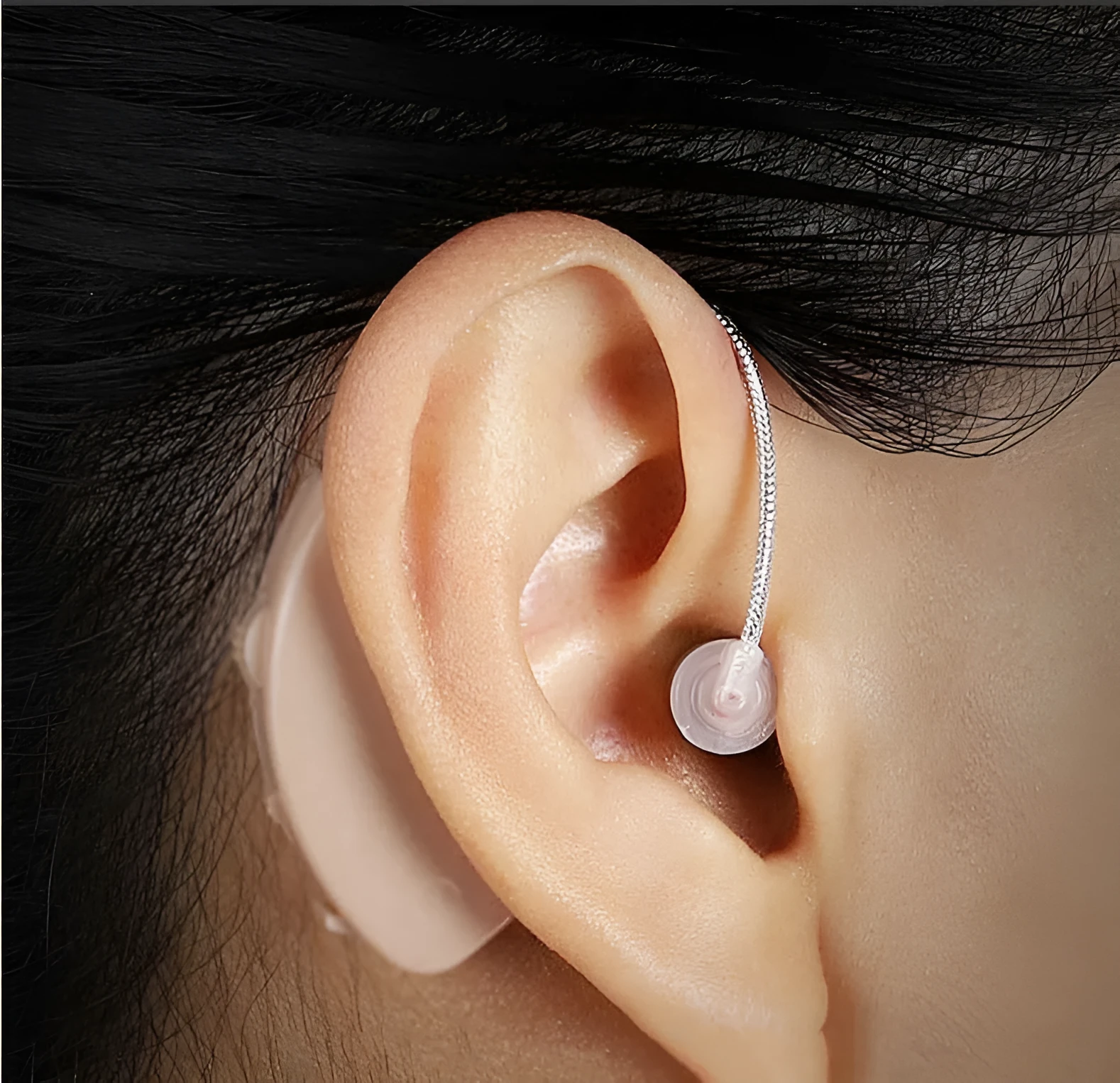 Black silicone rechargeable hearing aid amplifier with charging cable on a plain surface.