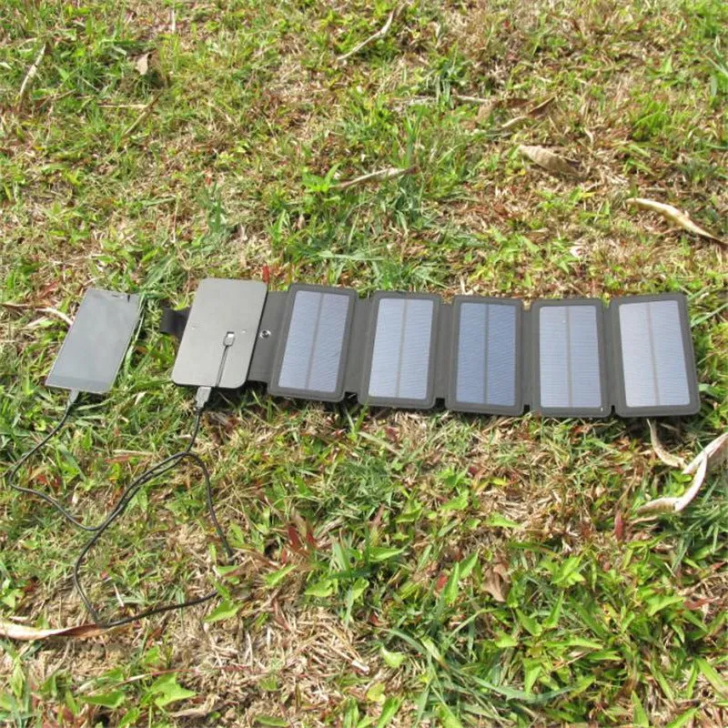 Black folding solar panel charger with monocrystalline cells and USB output, folded flat on a wooden surface, compass buckle visible