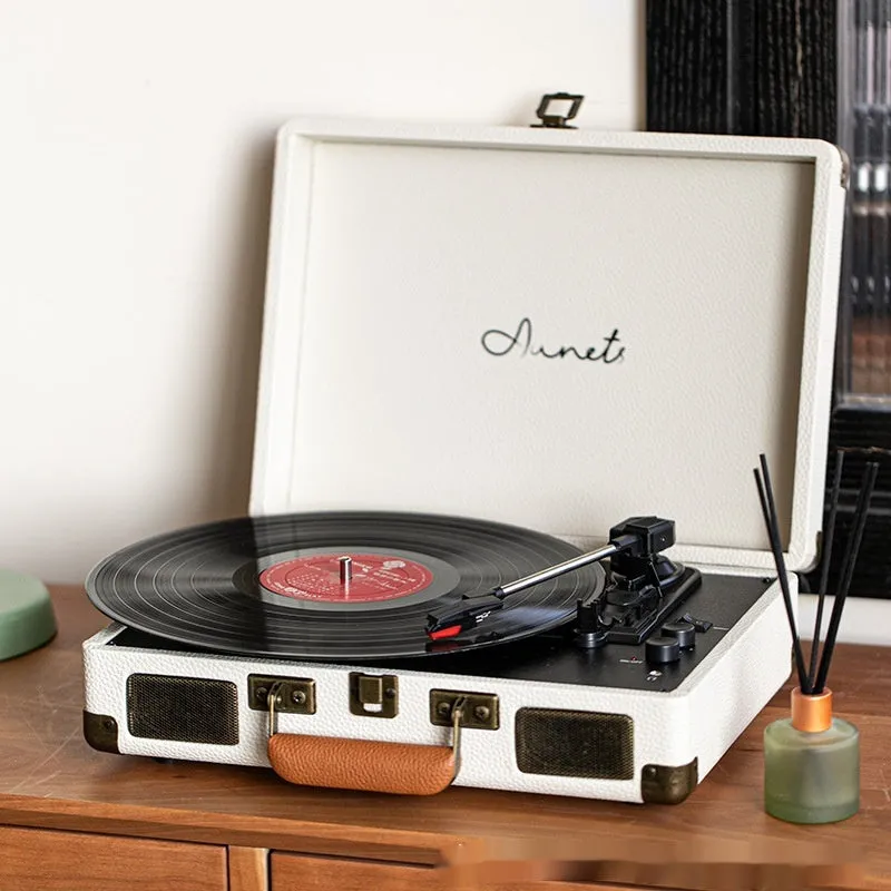 Cream-coloured retro phonograph in leather-effect suitcase with record on turntable and handle visible