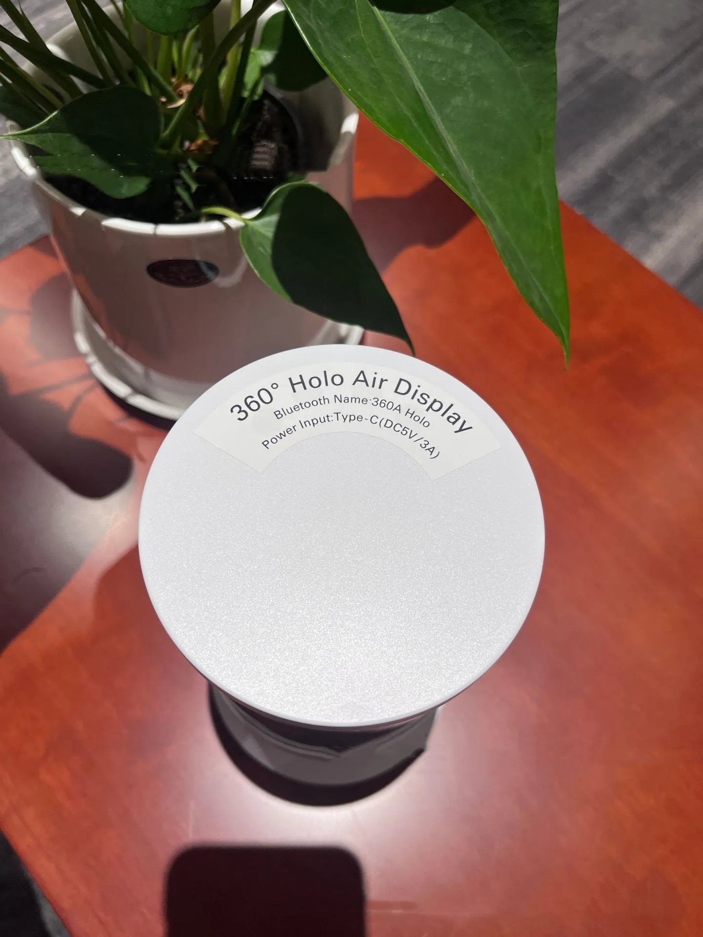 White 360-degree 3D holographic fan Bluetooth speaker with cylindrical screen on a desk