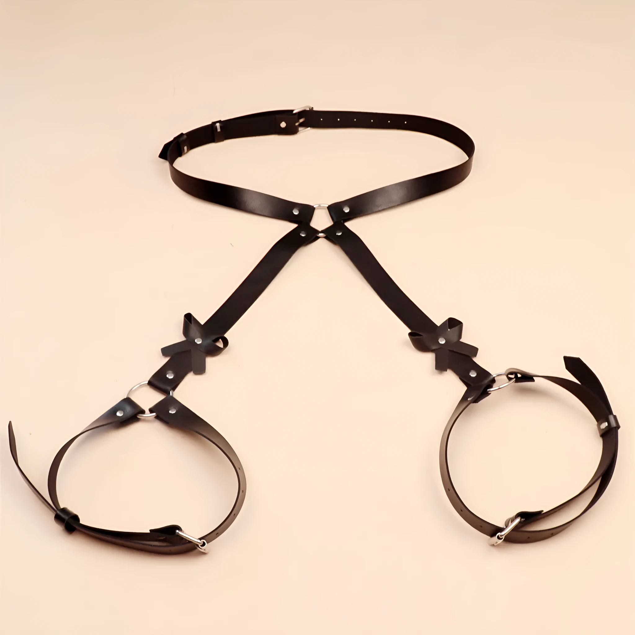 Black leather-look belt with metal buckle and bow detail, handcuffs from same set, on a dark surface