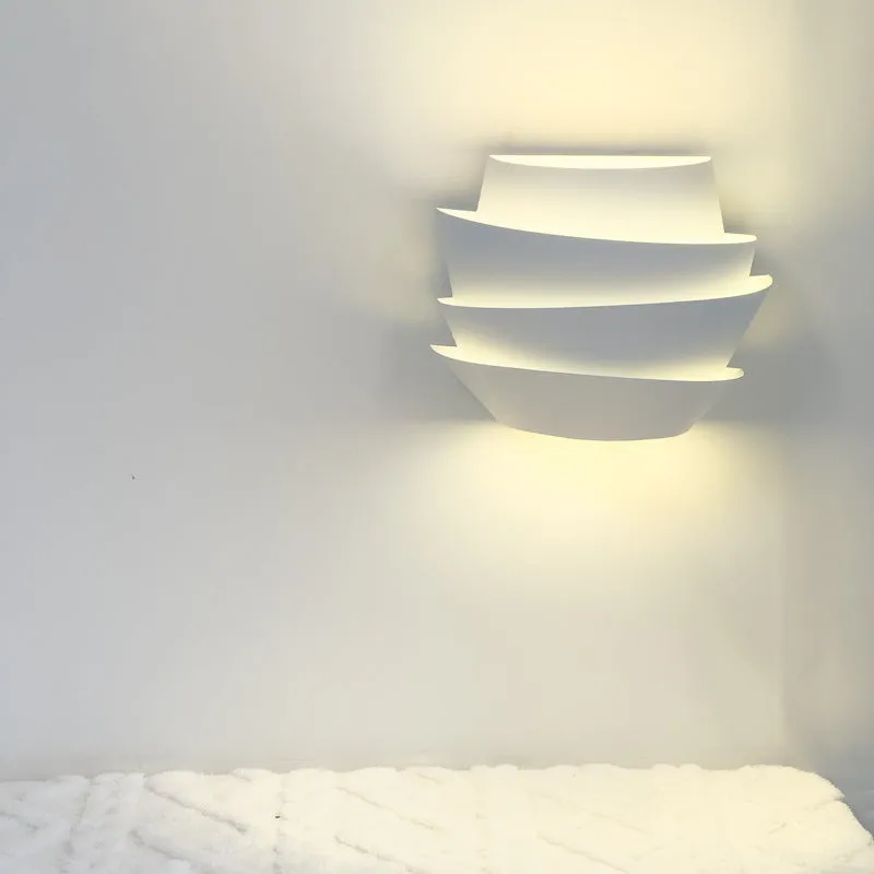 Modern white wall lamp with pine cone decoration mounted on a plain wall.