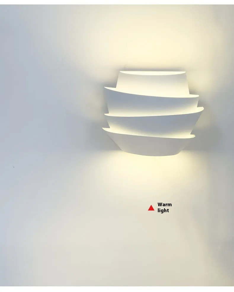 Modern white wall lamp with pine cone decoration mounted on a plain wall.
