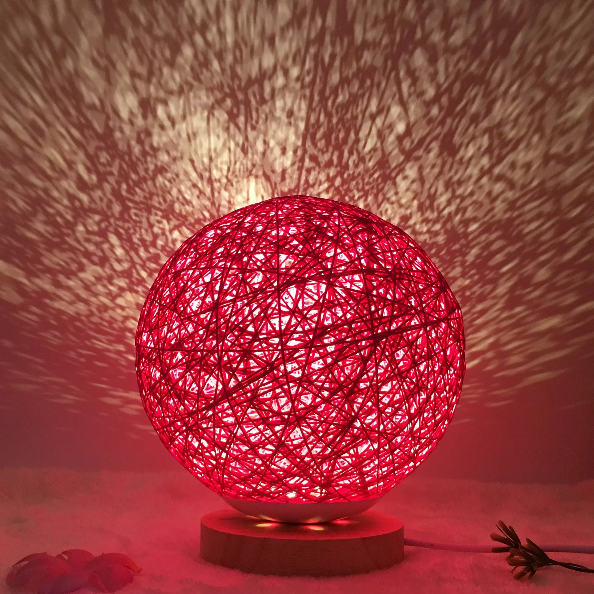 Hand-knit rattan ball table lamp with remote control on a wooden table, powered by USB cable.