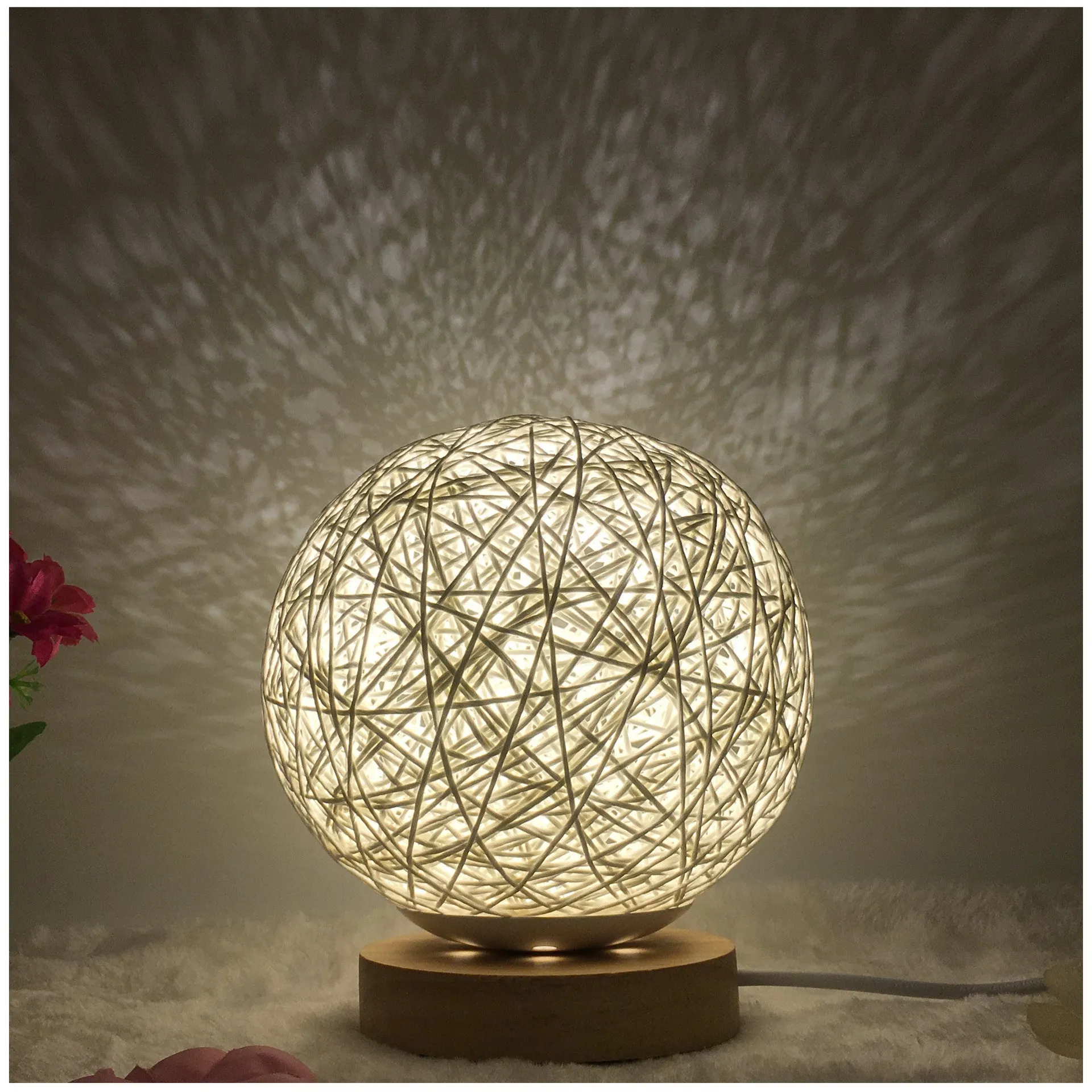 Hand-knit rattan ball table lamp with remote control on a wooden table, powered by USB cable.