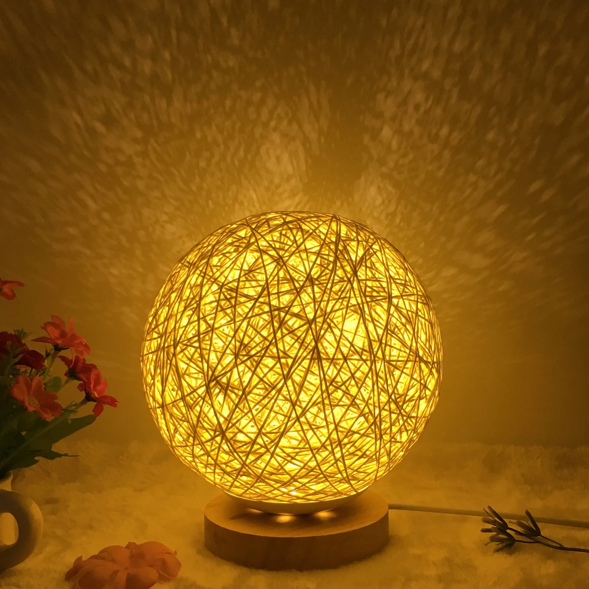 Hand-knit rattan ball table lamp with remote control on a wooden table, powered by USB cable.