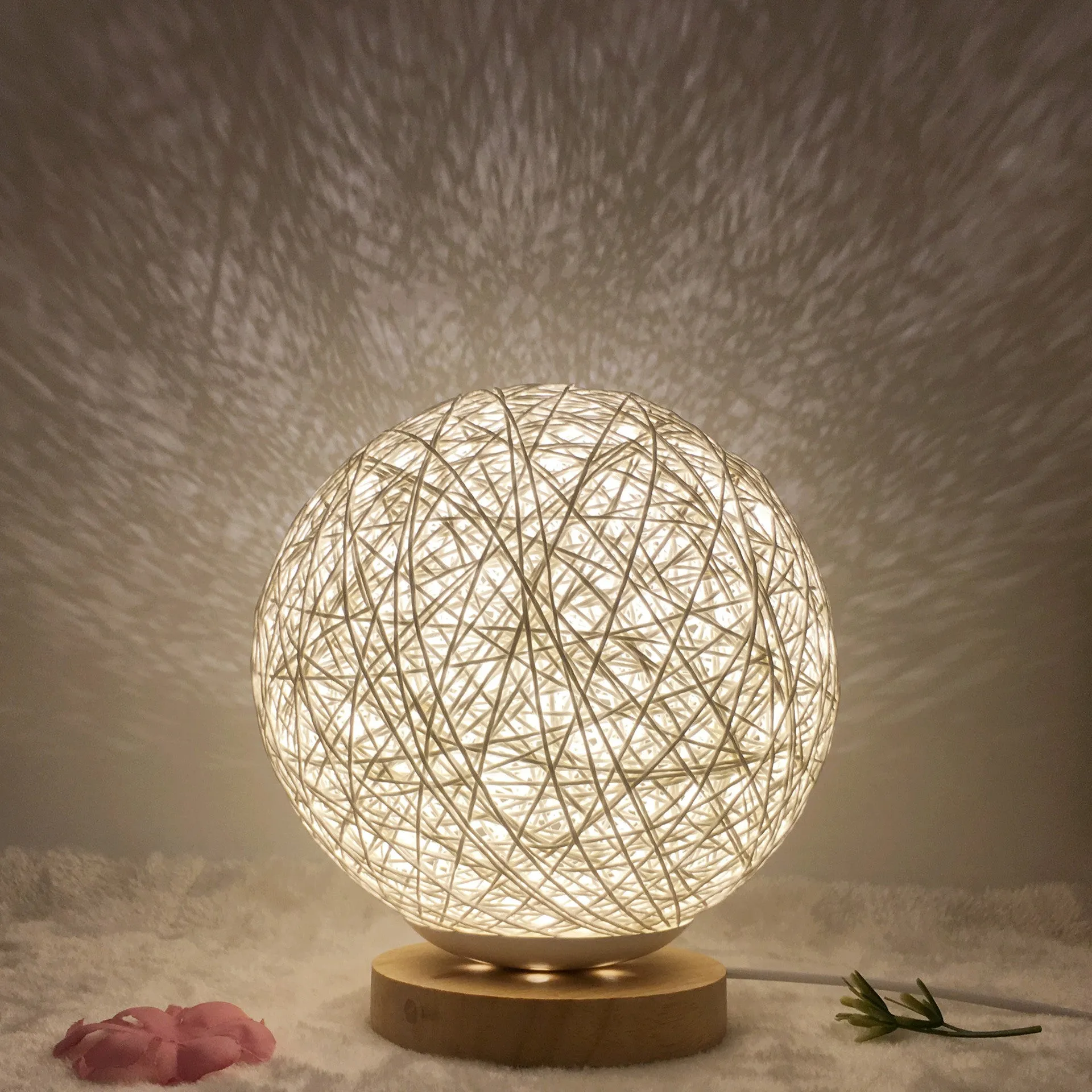 Hand-knit rattan ball table lamp with remote control on a wooden table, powered by USB cable.