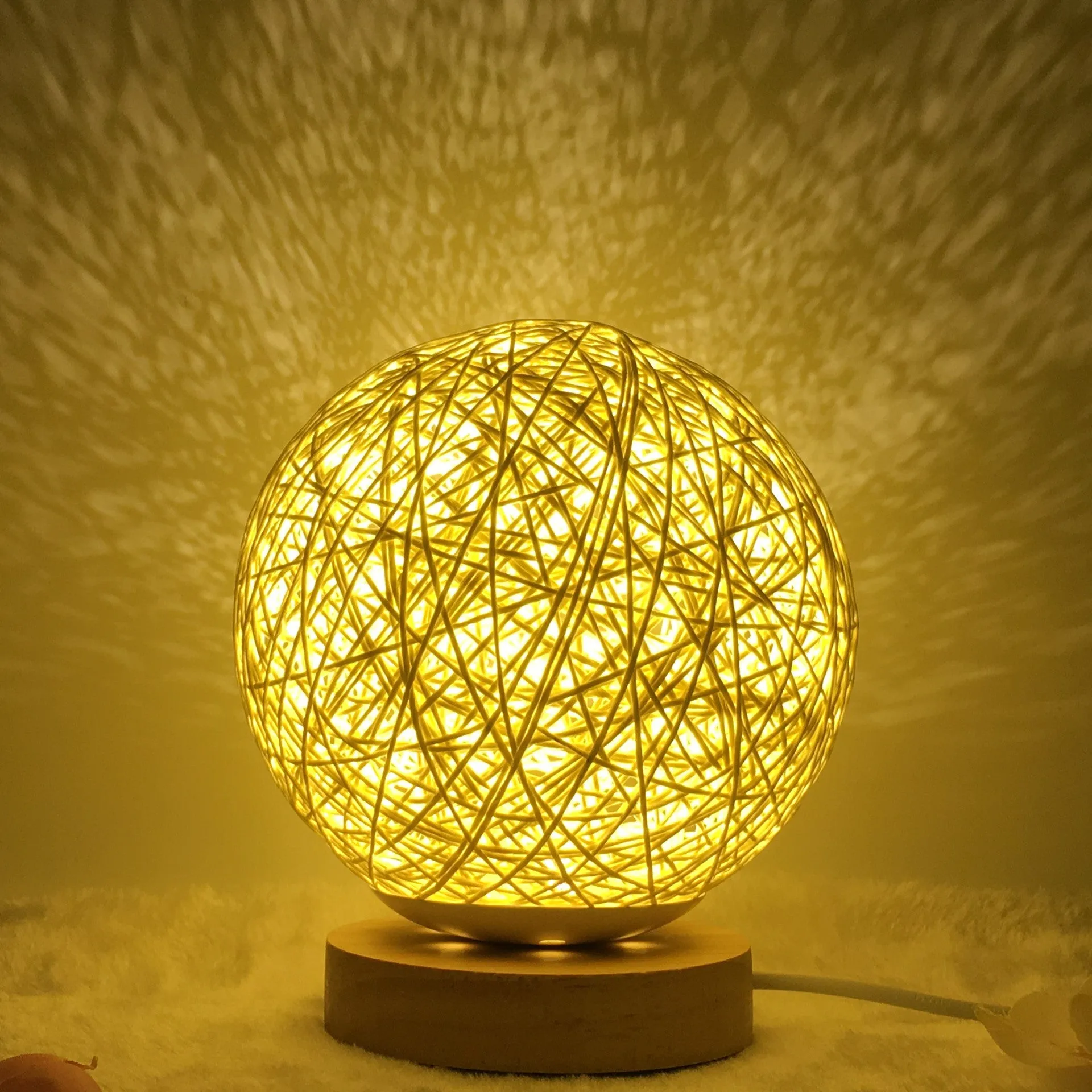 Hand-knit rattan ball table lamp with remote control on a wooden table, powered by USB cable.