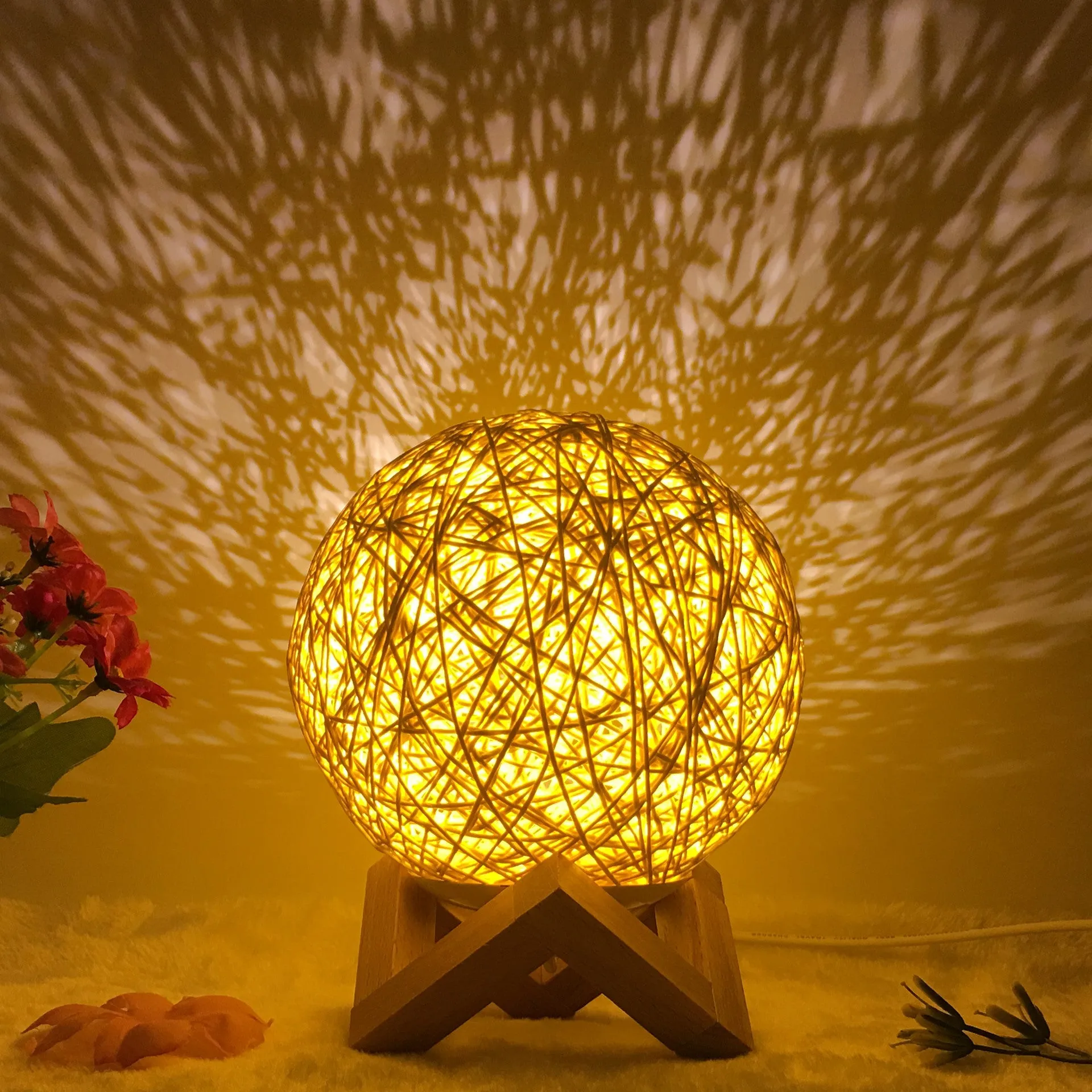 Hand-knit rattan ball table lamp with remote control on a wooden table, powered by USB cable.
