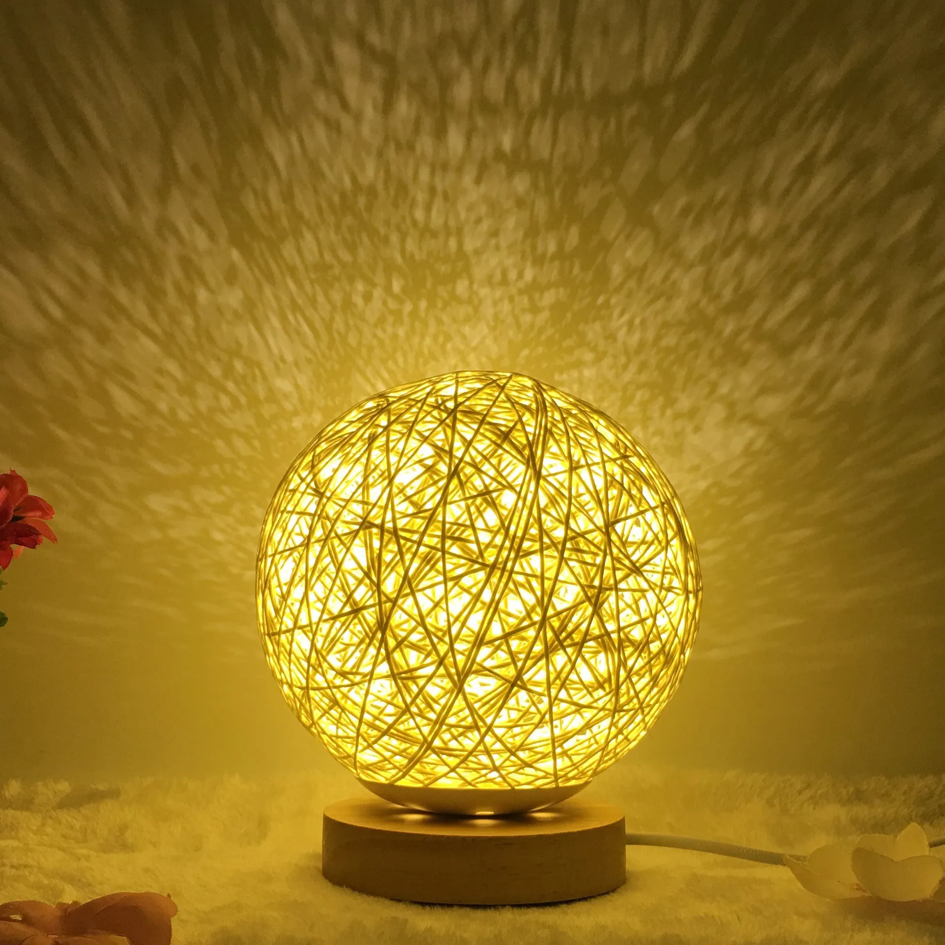 Hand-knit rattan ball table lamp with remote control on a wooden table, powered by USB cable.