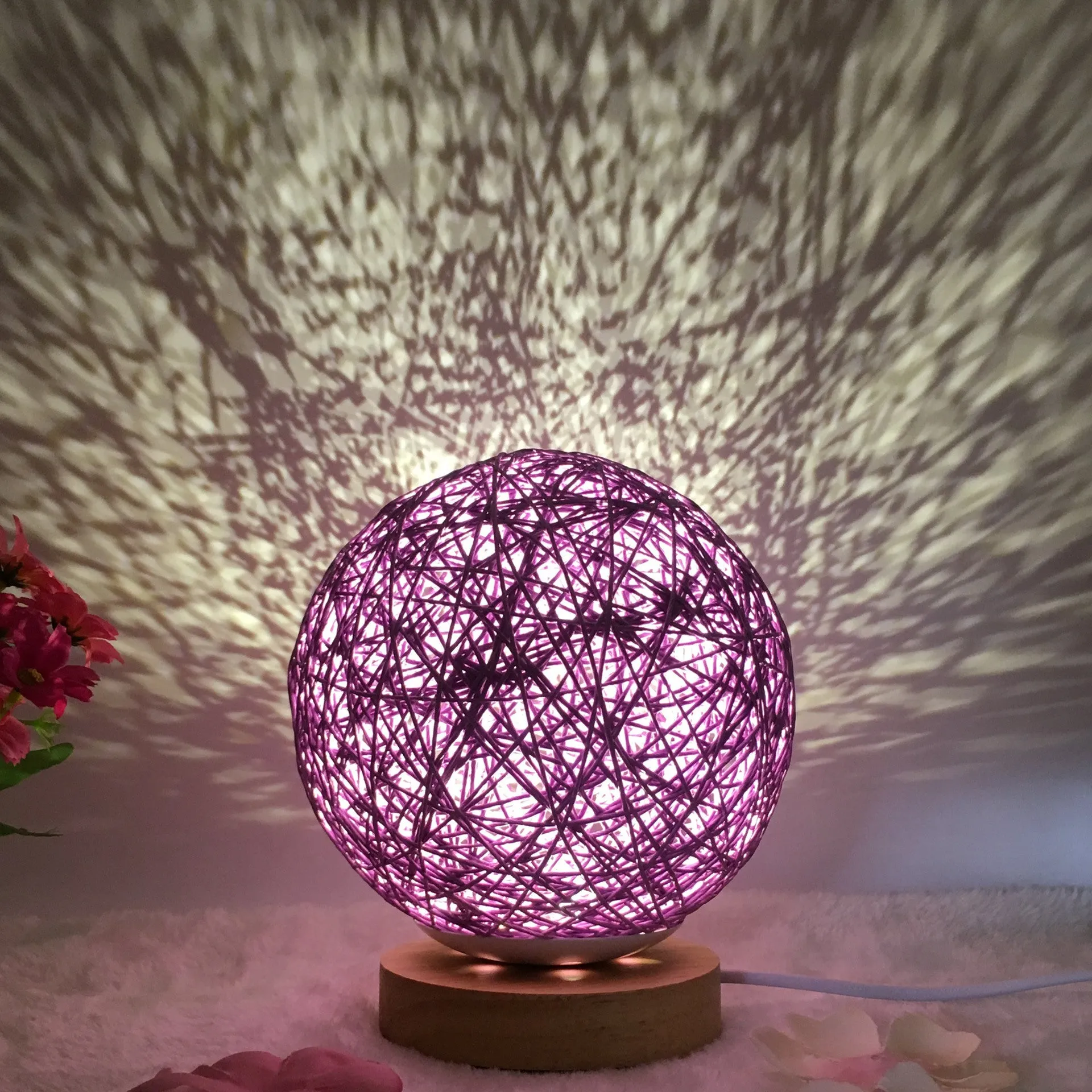Hand-knit rattan ball table lamp with remote control on a wooden table, powered by USB cable.