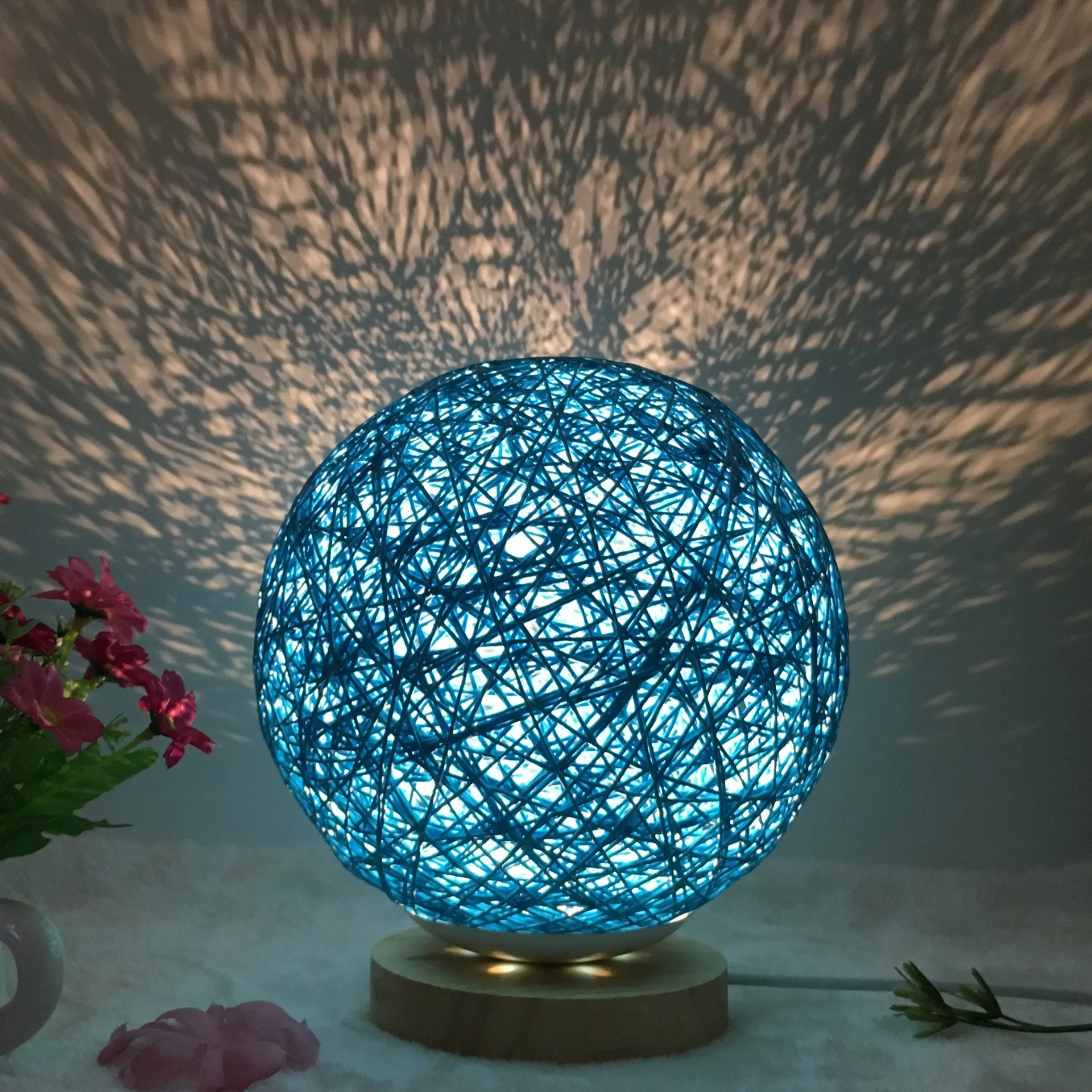 Hand-knit rattan ball table lamp with remote control on a wooden table, powered by USB cable.
