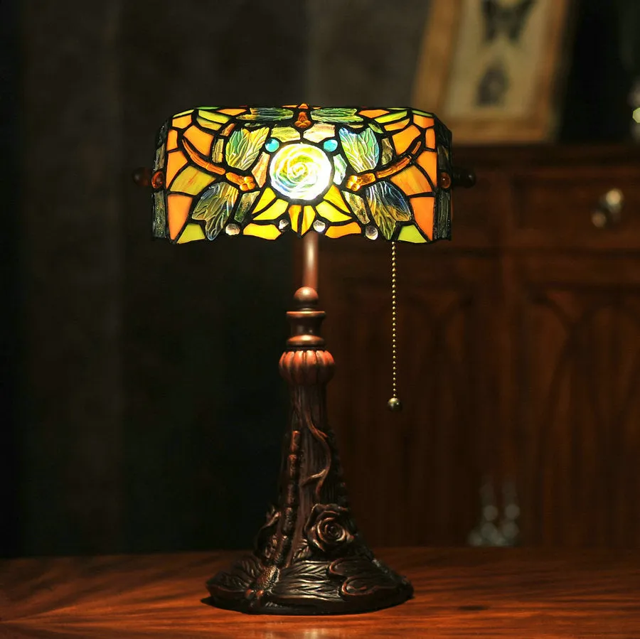 Tiffany style table lamp with coloured stained glass shade and resin base on a desk.