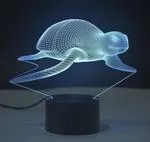 Small 3D acrylic LED table lamp on black base displaying multi-coloured gradient light, with remote control.