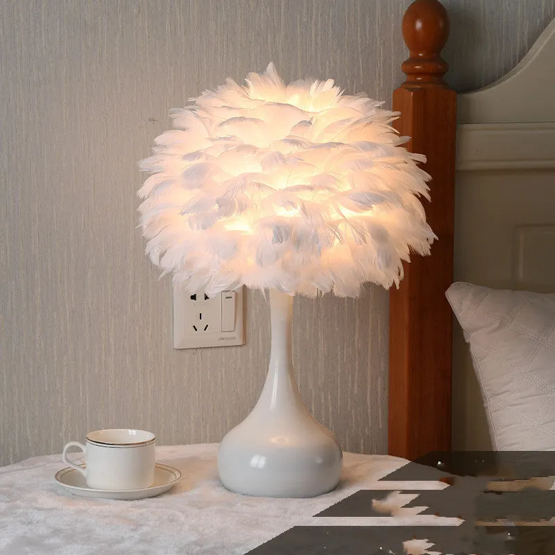 White feather table lamp with hand-woven fur shade and iron base on a wooden bedside table.