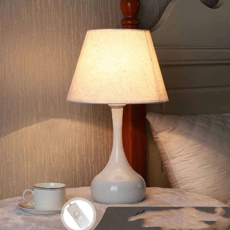 White feather table lamp with hand-woven fur shade and iron base on a wooden bedside table.