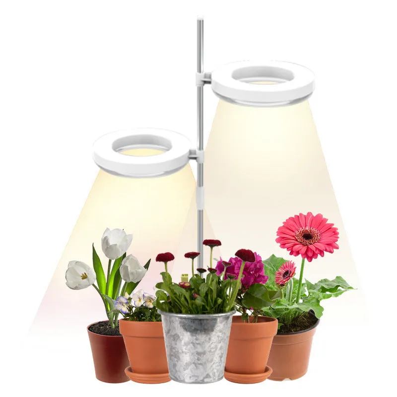 A white clamp-on plant growth lamp with an adjustable head, positioned next to small indoor potted plants on a desk.