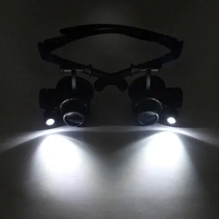 Black hands-free magnifier glasses with LED lights and four pairs of interchangeable magnification lenses on a workbench.