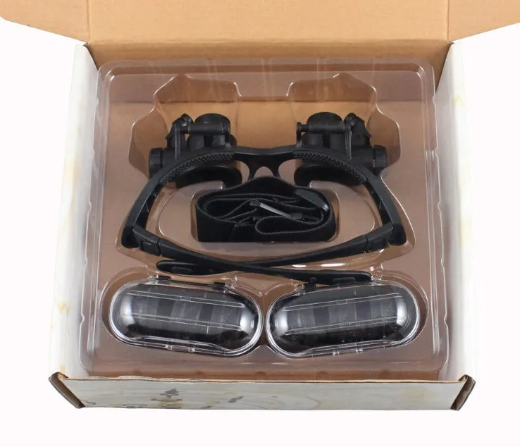 Black hands-free magnifier glasses with LED lights and four pairs of interchangeable magnification lenses on a workbench.