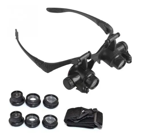 Black hands-free magnifier glasses with LED lights and four pairs of interchangeable magnification lenses on a workbench.