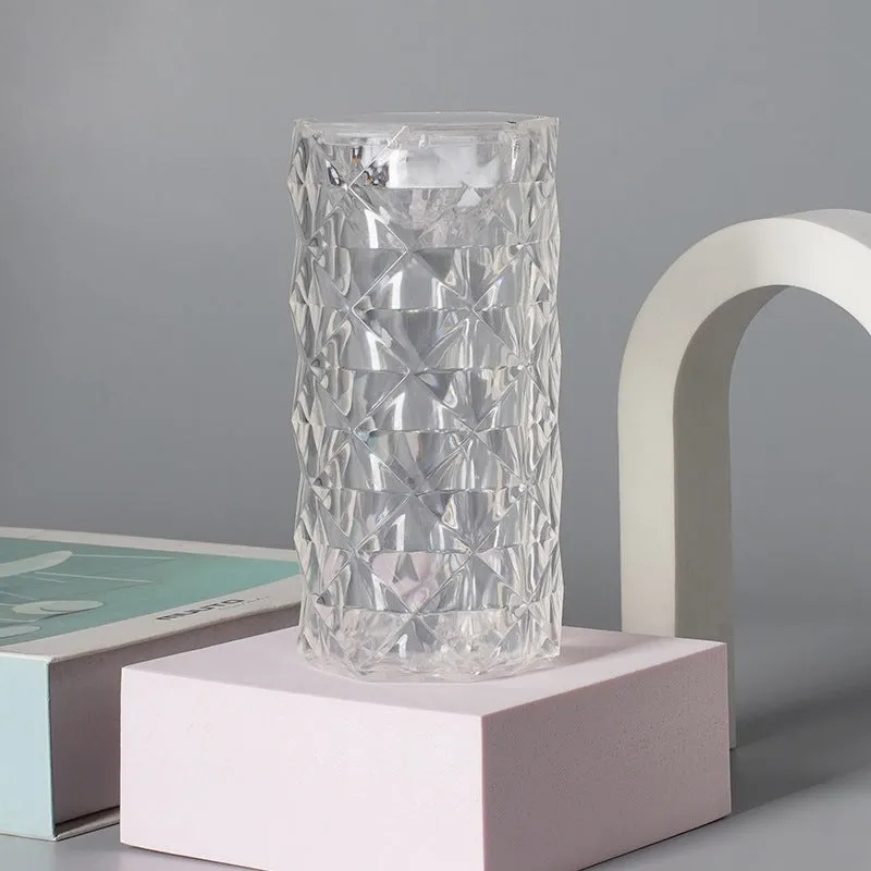 Rose atmosphere crystal bedside lamp with plastic lampshade emitting soft yellow light on a wooden table