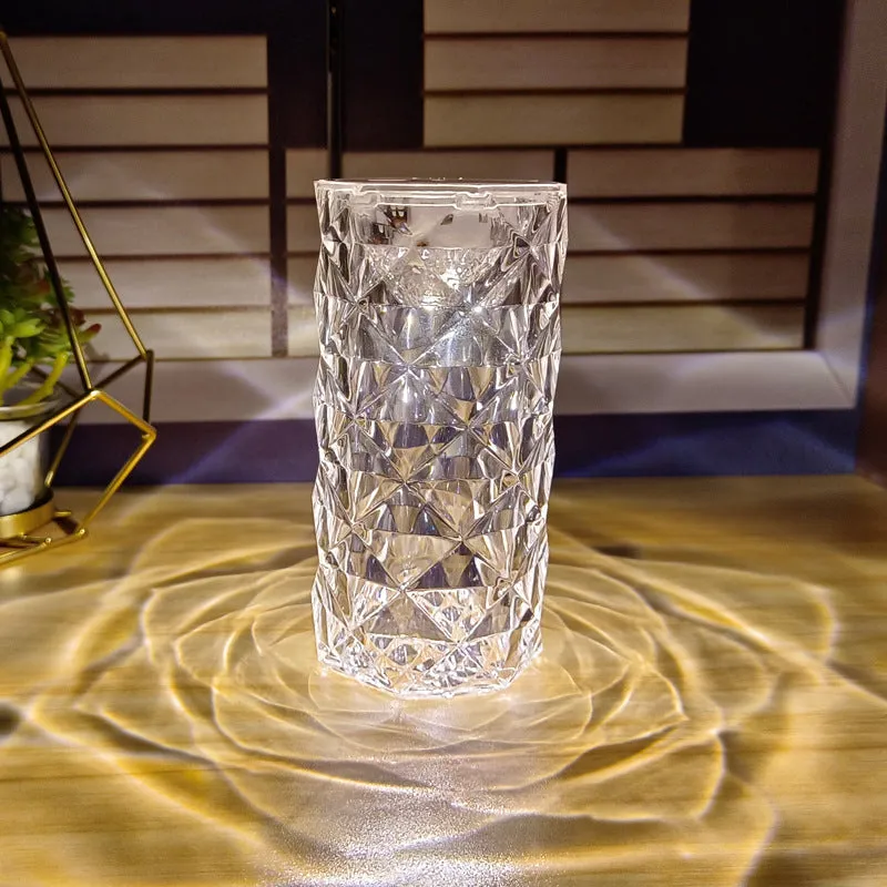 Rose atmosphere crystal bedside lamp with plastic lampshade emitting soft yellow light on a wooden table