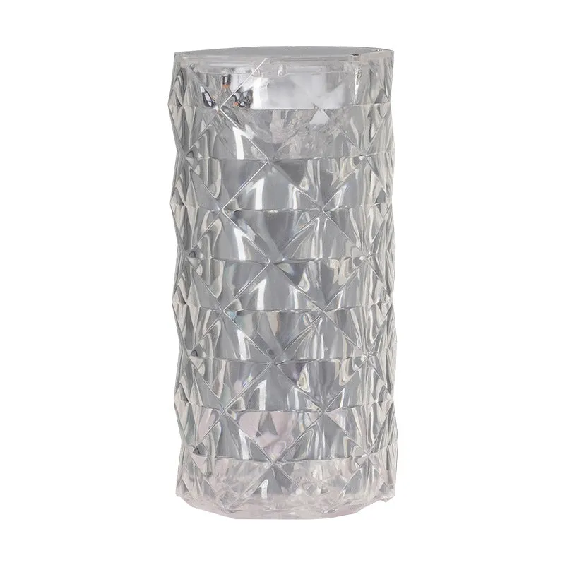 Rose atmosphere crystal bedside lamp with plastic lampshade emitting soft yellow light on a wooden table